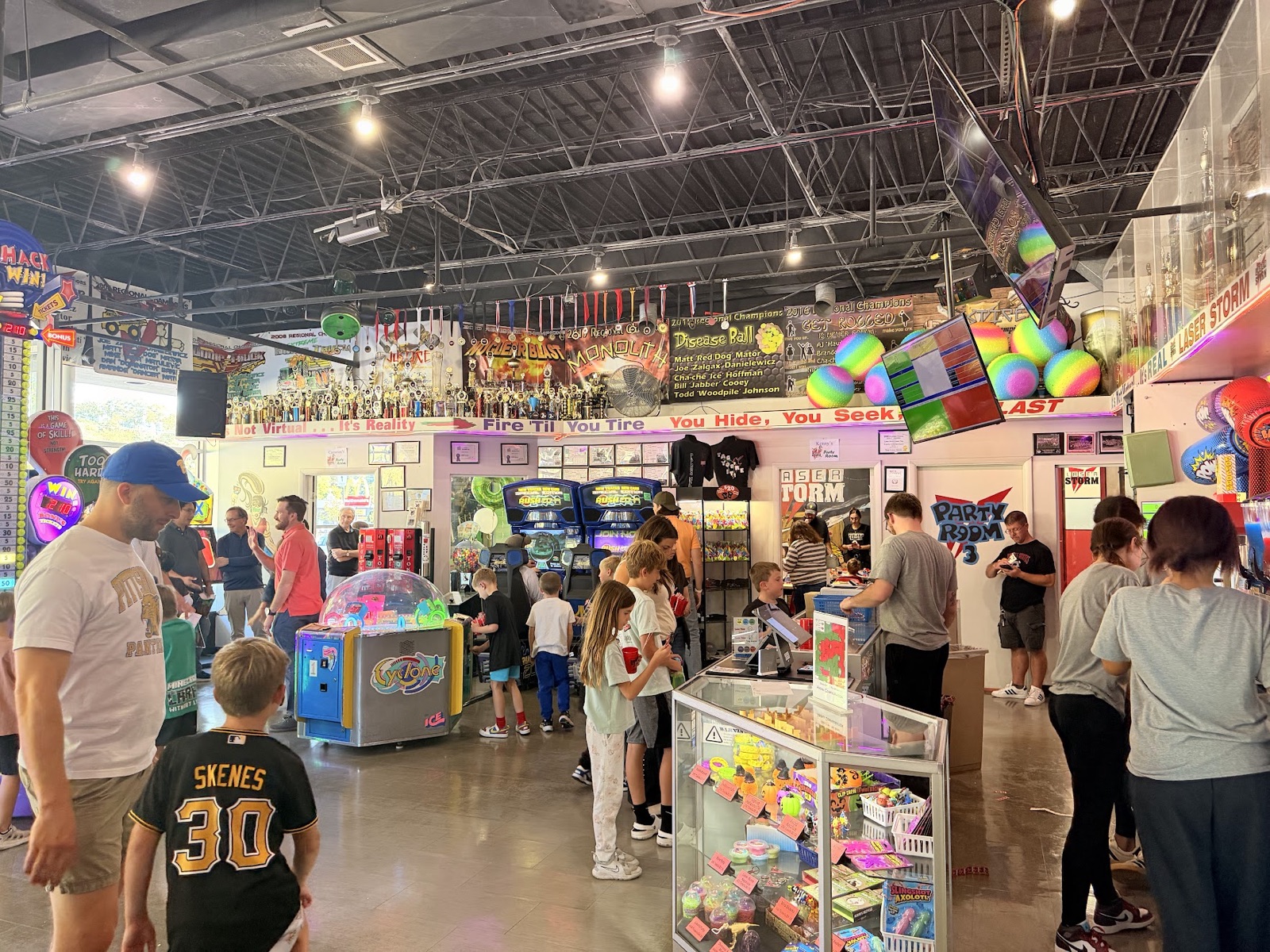 The busy arcade floor, with kids and parents milling around prize counters, claw machines, and arcade cabinets