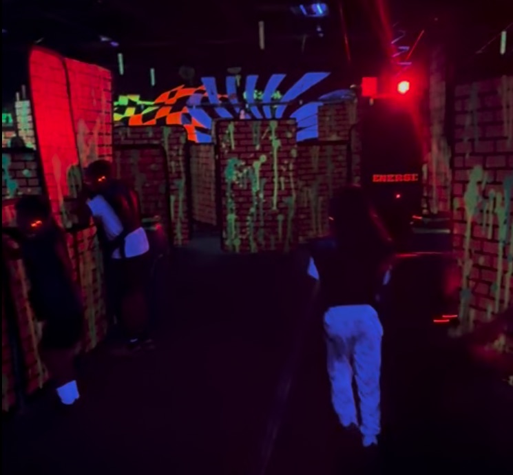 Kids running through the dark, blacklit arena past painted brick barriers