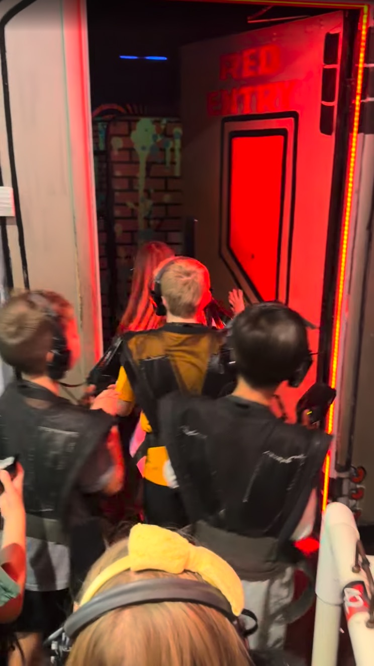 Kids in laser tag vests and headsets lining up at a red-lit door into the arena