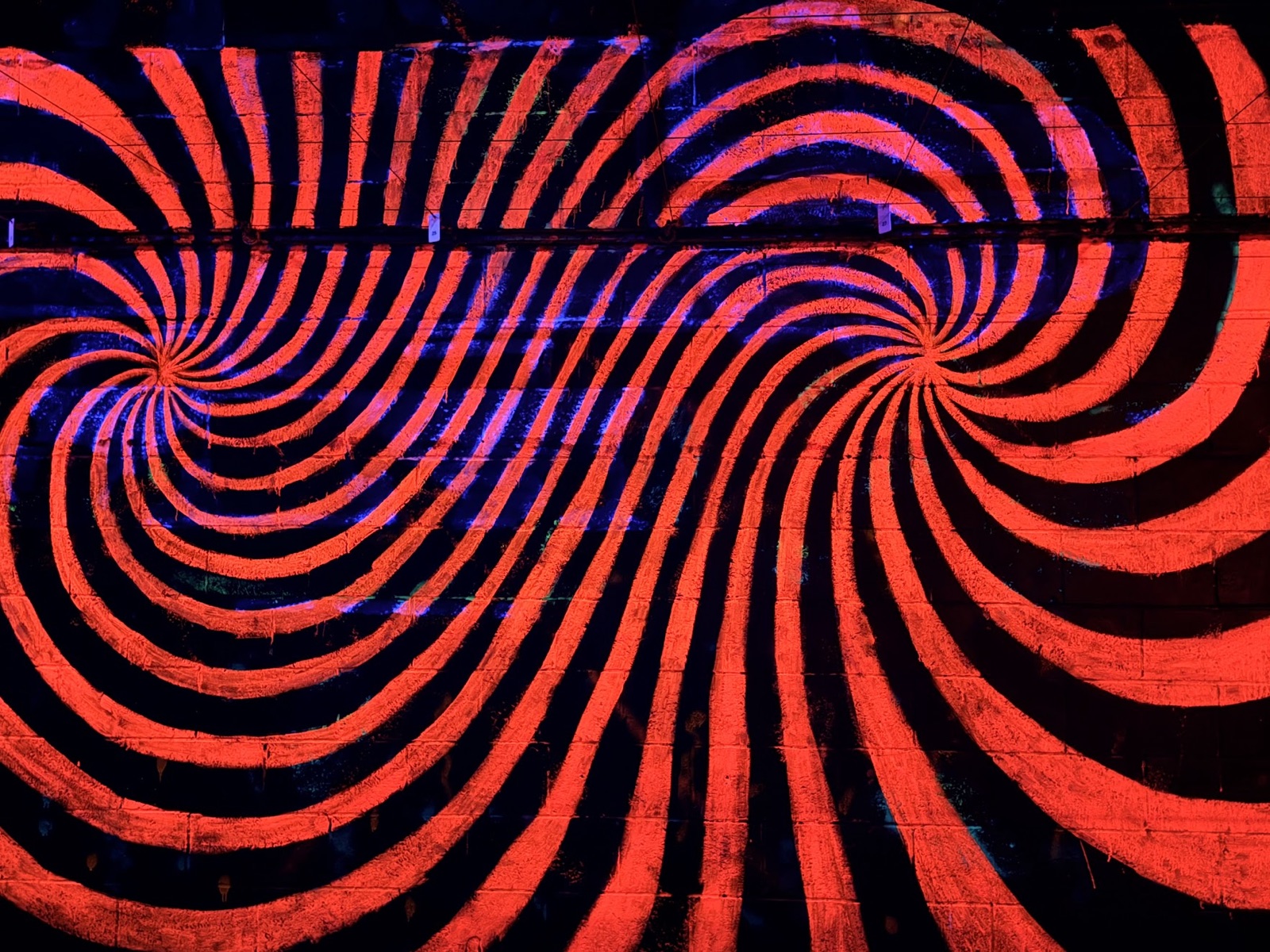 A blacklit wall painted with two red-and-black swirling spirals